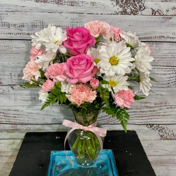 Pink roses and white daisies in a clear glass vase with a pink ribbon