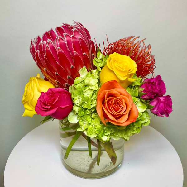 Colorful bouquet with roses, hydrangea, and a protea in a glass vase