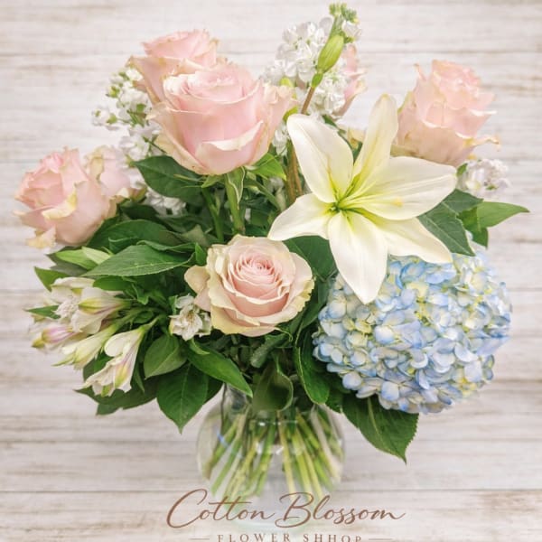 Pink roses and white lilies in a glass vase with blue hydrangea