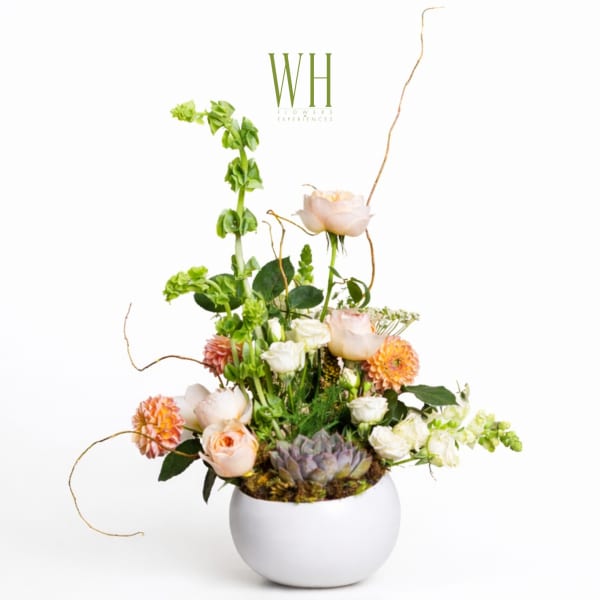 Tall floral arrangement in a white round vase with peach and white blooms