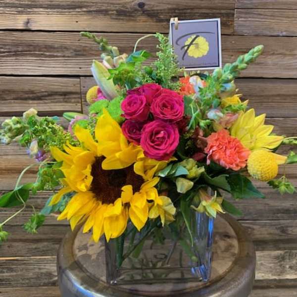 Bright mixed bouquet with sunflowers, pink roses, and yellow blooms in a glass vase.