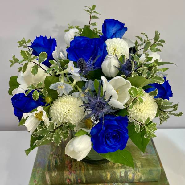 Blue and white flower arrangement in a glass vase on stacked decorative boxes