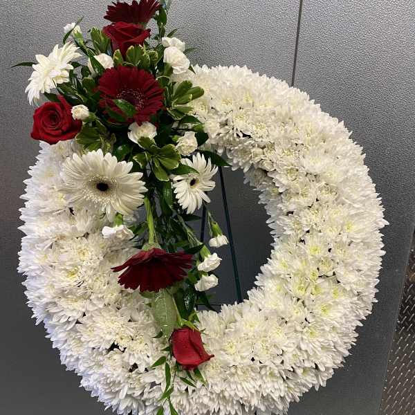 Circular white floral wreath with red roses and burgundy daisies
