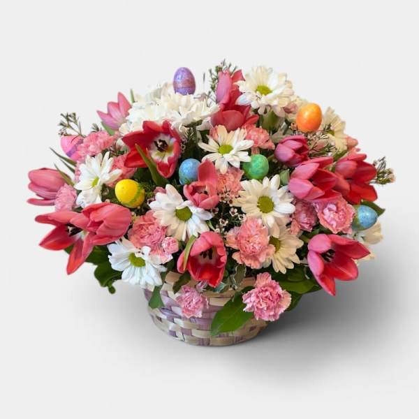 Pink tulips, white daisies, and carnations in a basket with colorful Easter eggs.