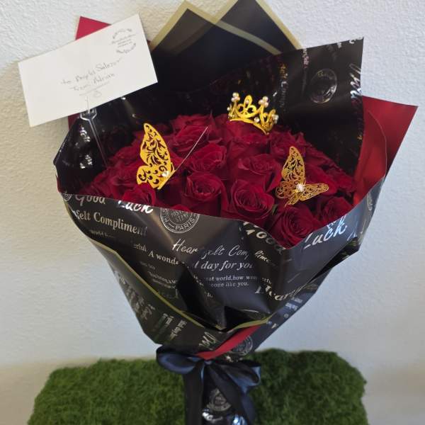 Bouquet of red roses wrapped in black paper with a small crown topper