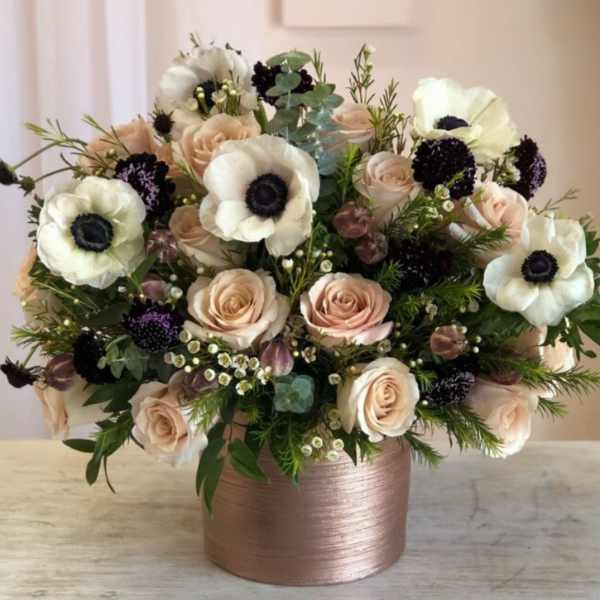 Arrangement of blush roses, white anemones, and dark blooms in a rose gold cylinder vase