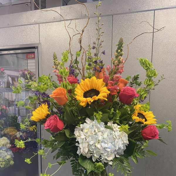 Tall mixed bouquet with sunflowers, roses, and white hydrangea in a glass vase