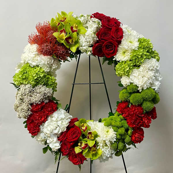 Large floral wreath with red roses, white blooms, and green orchids on a black stand