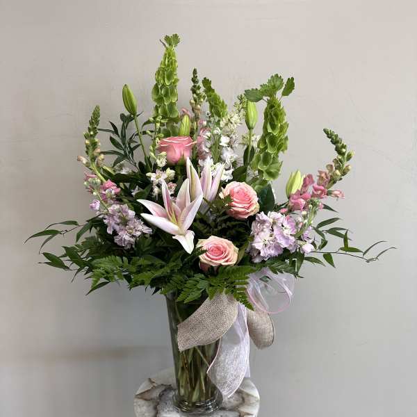 Pink lilies and roses in a glass vase with green spikes