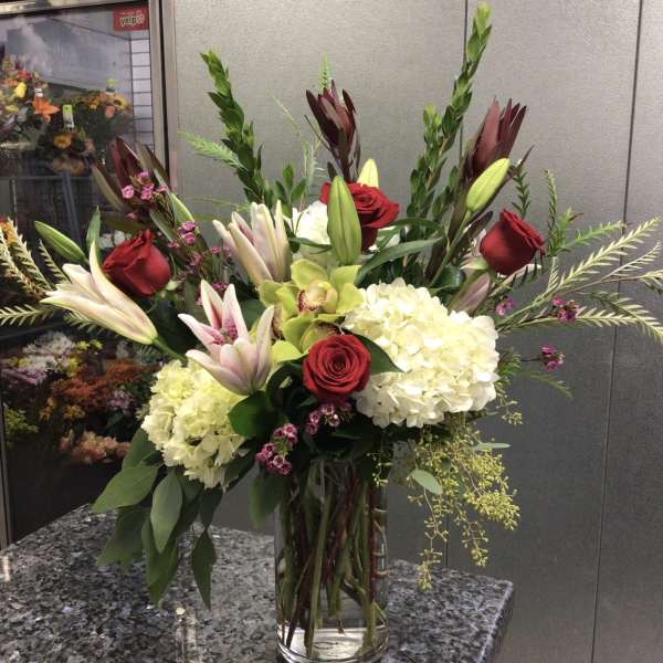 Tall bouquet of red roses, lilies, and white hydrangeas in a glass vase