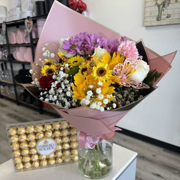 Mixed bouquet in pink wrap with sunflowers, roses, and purple daisies