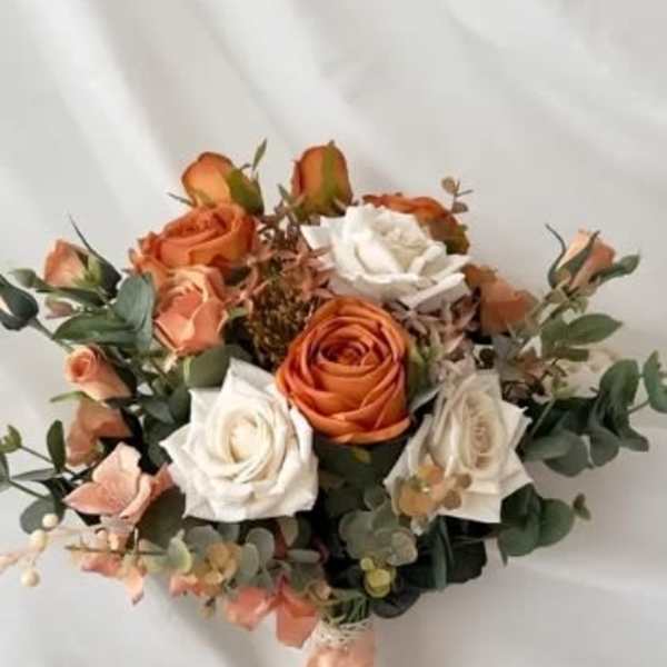 Bouquet of orange and white roses with greenery and a peach ribbon