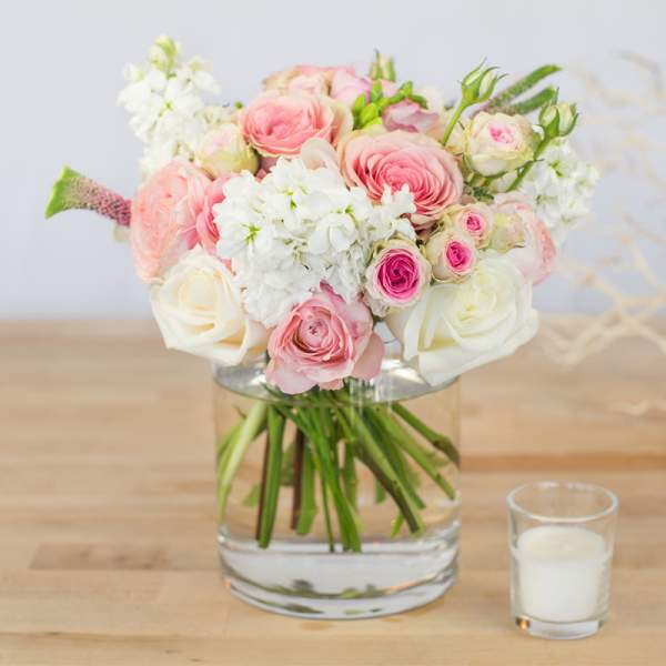 Pink and white rose bouquet in a clear glass vase with a candle beside it