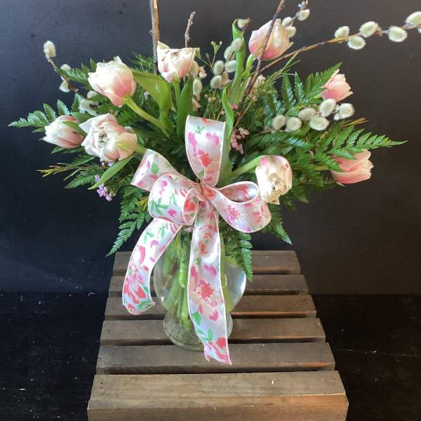 Pink and white tulips in a glass vase with a floral ribbon