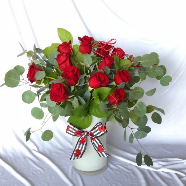 Red roses in a white vase with eucalyptus and a striped ribbon bow