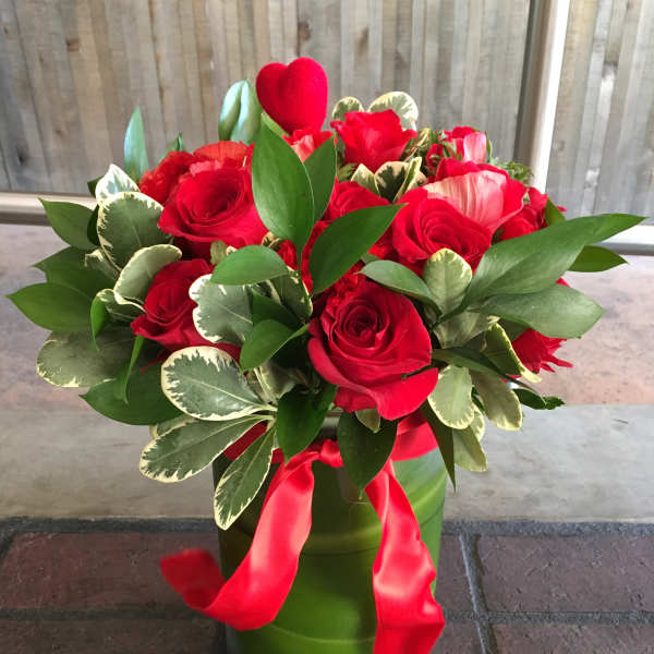 Red roses arranged in a green vase with a red ribbon