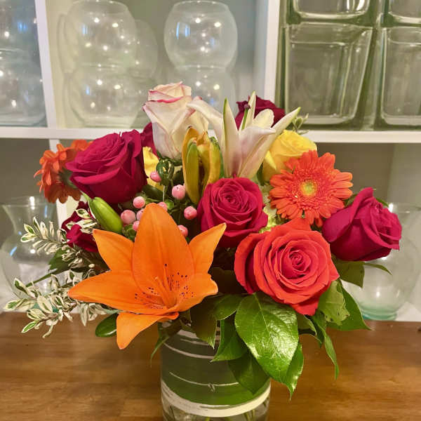 Mixed bouquet of roses, lilies, and a gerbera daisy in a glass vase