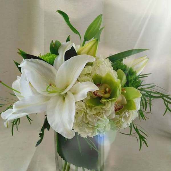 White lilies and green orchids in a clear glass vase