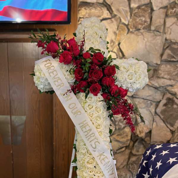 Cross-shaped floral tribute of red and white roses with a memorial ribbon