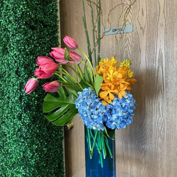 Pink tulips with blue and yellow flowers in a tall blue vase
