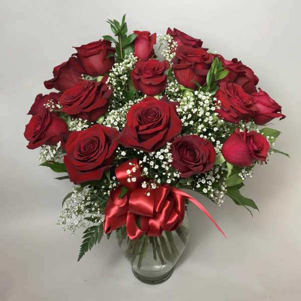 Bouquet of red roses with baby's breath in a clear glass vase and red ribbon