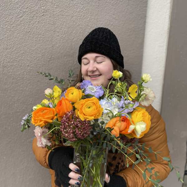 Person holding a colorful bouquet in a clear glass vase