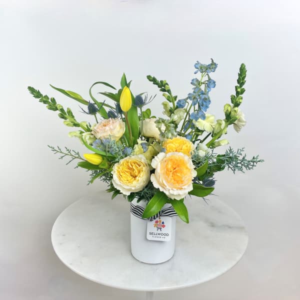 Mixed bouquet in a white vase with yellow, blue, and cream flowers