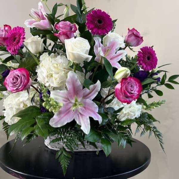Basket arrangement of pink lilies, roses, gerbera daisies, and white hydrangeas in a white wicker container