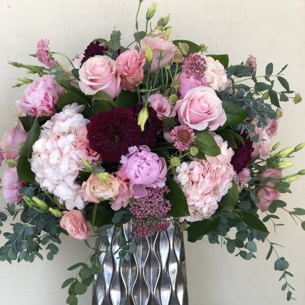 Tall arrangement of pink and burgundy flowers in a silver textured vase