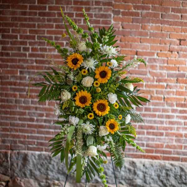 Tall floral standing spray with sunflowers and white blooms on an easel