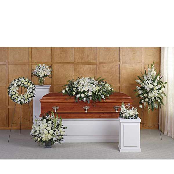 Set of white floral funeral arrangements around a wooden casket in a chapel.