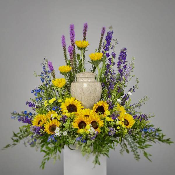 Cremation floral display with yellow sunflowers and purple blooms surrounding a stone urn