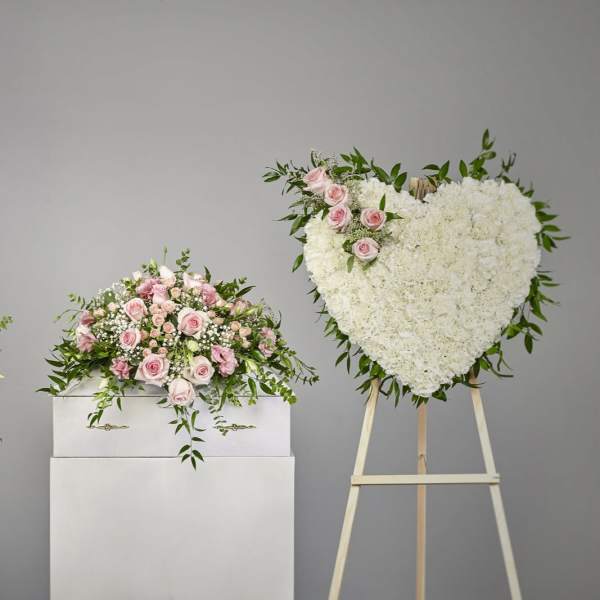 Sympathy set with pink and white arrangements and a white heart wreath on a stand
