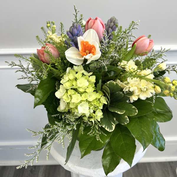 Spring bouquet with pink tulips, white daffodil, green hydrangea, and purple hyacinths in a white container