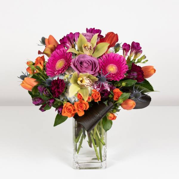 Mixed bouquet of pink, orange, and purple flowers in a clear glass vase