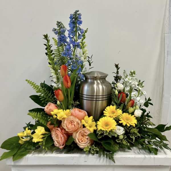 Floral urn arrangement with blue delphinium, tulips, roses, and yellow daisies
