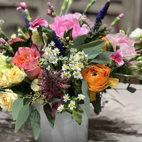 Colorful mixed arrangement of pink roses, yellow blooms, daisies and orange ranunculus in a white vase