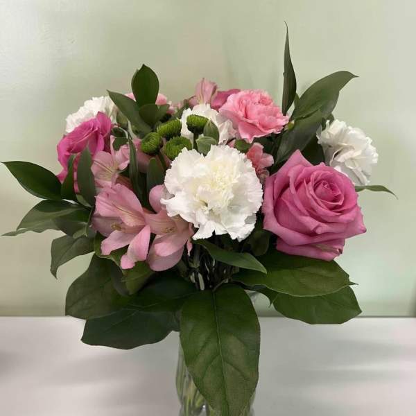 Mixed bouquet of pink roses, carnations, alstroemeria, and white blooms in a clear glass vase