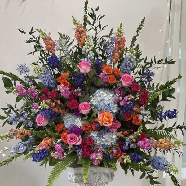 Large mixed floral arrangement with roses, hydrangeas, and snapdragons in a pedestal vase