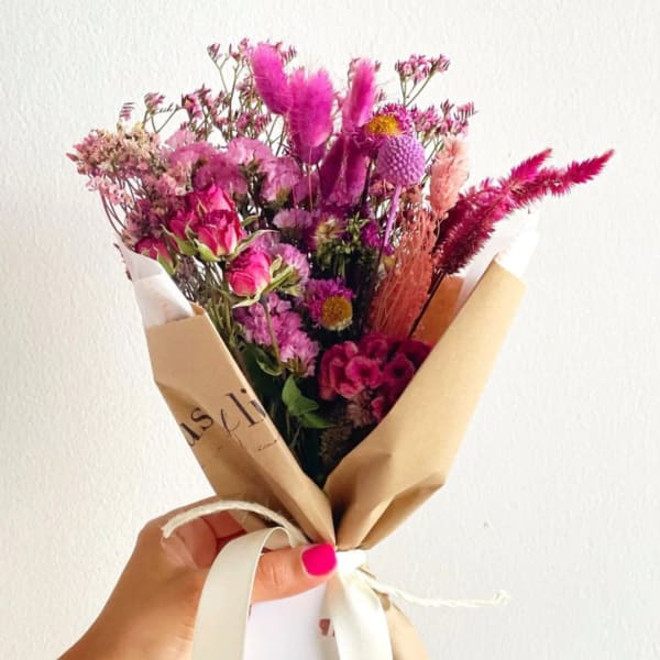 Handheld bouquet of pink and purple dried flowers wrapped in brown paper