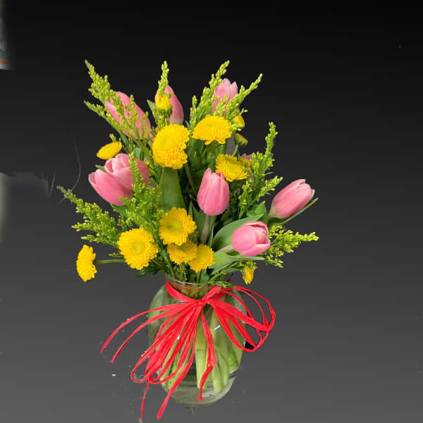 Pink tulips and yellow chrysanthemums in a glass vase with a red ribbon