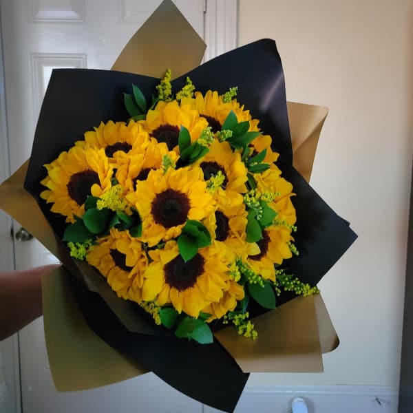 Hand-tied bouquet of bright yellow sunflowers wrapped in black and gold paper.