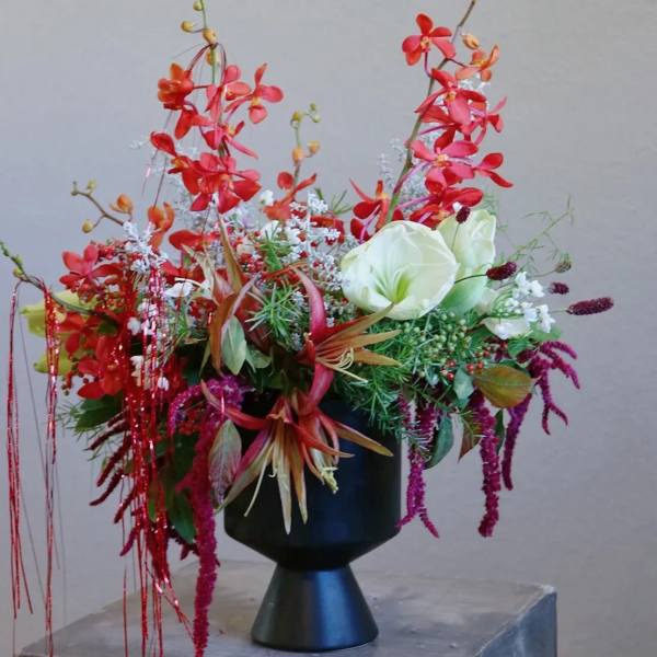 Tall floral arrangement with red orchids and white blooms in a black vase