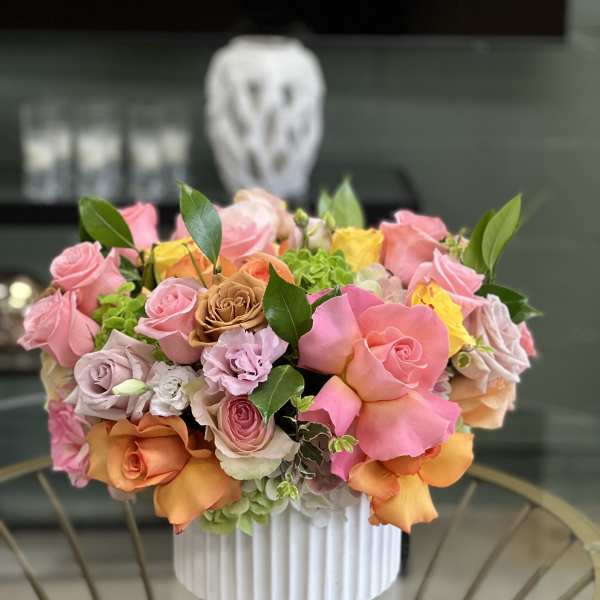 Mixed pink, peach, and yellow roses arranged in a white vase