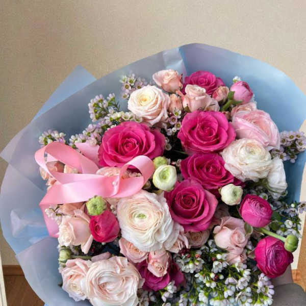 Bouquet of pink and white roses wrapped in blue paper with a pink ribbon