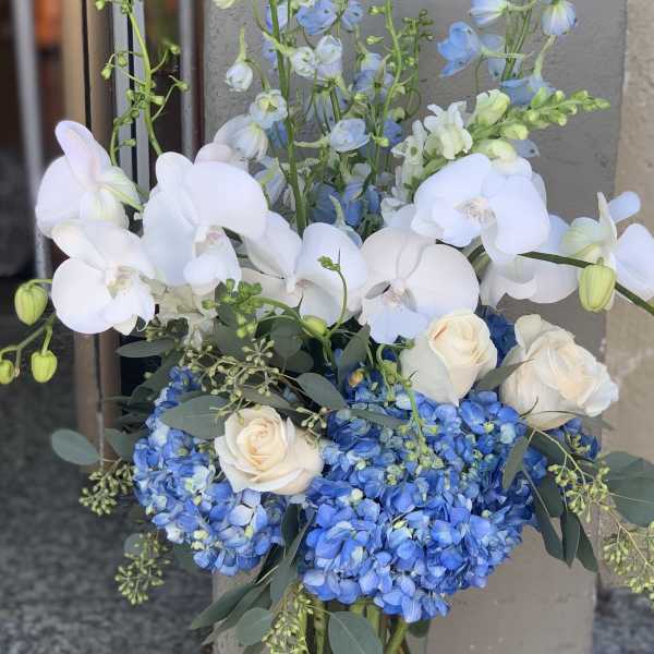 Blue hydrangeas, white orchids, and cream roses in a glass vase