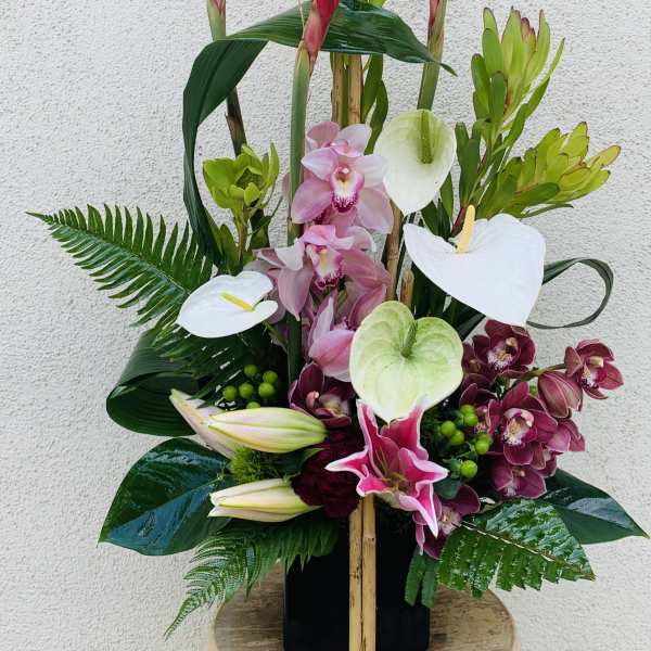 Tropical floral arrangement with pink orchids and white anthuriums in a black vase