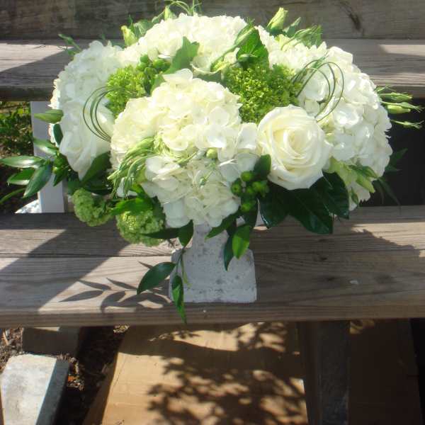 White floral arrangement in a stone vase with roses and hydrangeas