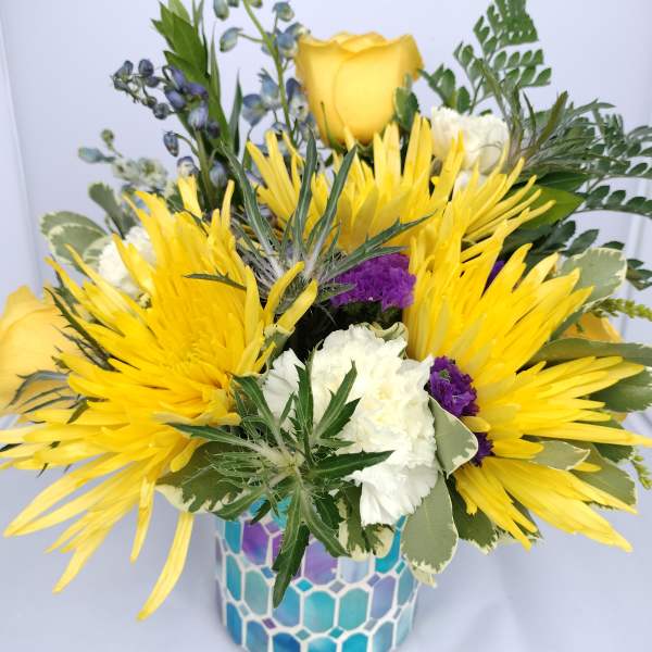 Yellow roses and white flowers in a blue mosaic vase