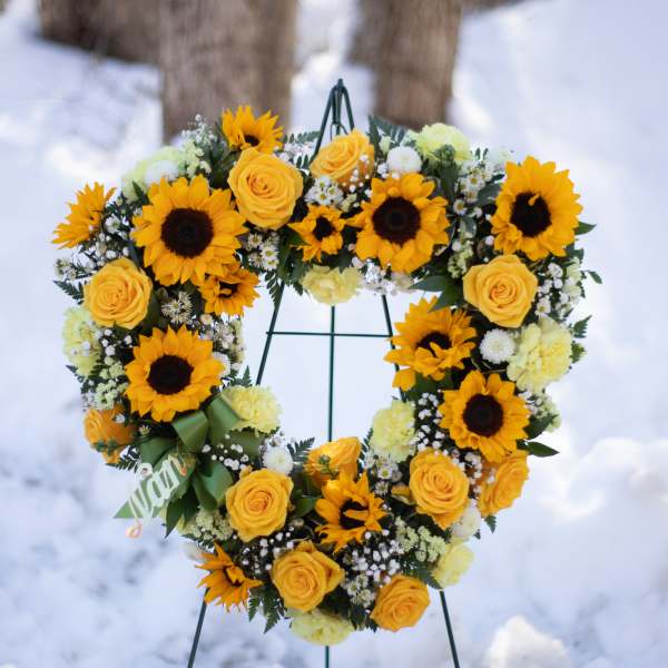 Heart-shaped wreath of yellow roses and sunflowers on a stand